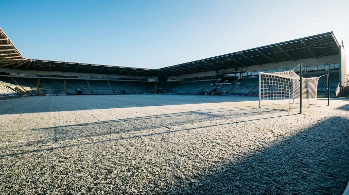 Campo de fútbol profesional vacío con césped cubierto de escarcha en un día invernal soleado